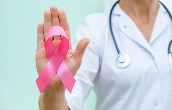 Pink ribbon for breast cancer awareness in doctor's hand, women breast tumor illness campaign. Closeup view