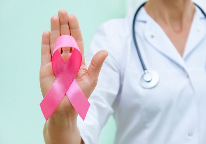 Pink ribbon for breast cancer awareness in doctor's hand, women breast tumor illness campaign. Closeup view