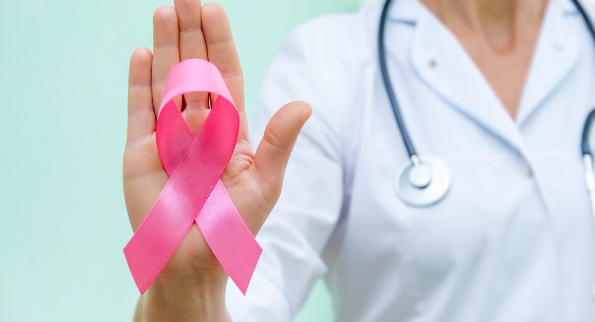 Pink ribbon for breast cancer awareness in doctor's hand, women breast tumor illness campaign. Closeup view